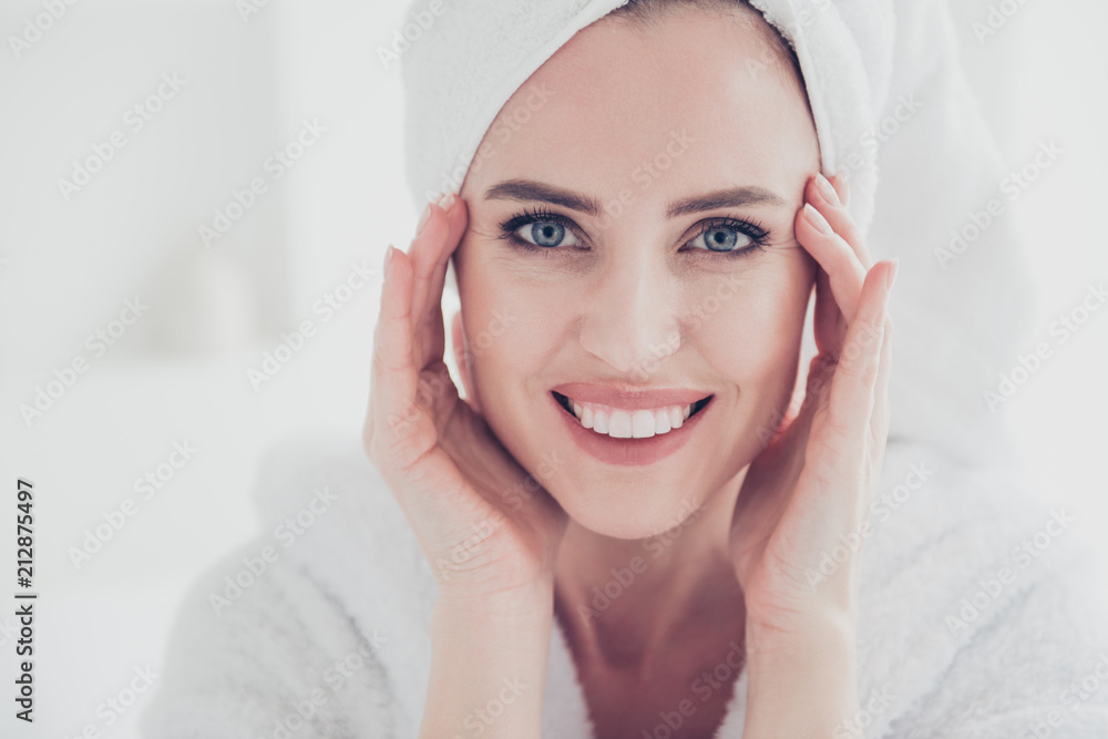 Close up portrait of young cute adult woman looking straight at camera smiling with her teeth wearing white bathrobe and turban keeping hands and fingers near eyes wrinkles in white interior Close up portrait of young cute adult woman looking straight at camera smiling with her teeth wearing white bathrobe and turban keeping hands and fingers near eyes wrinkles in white interior
