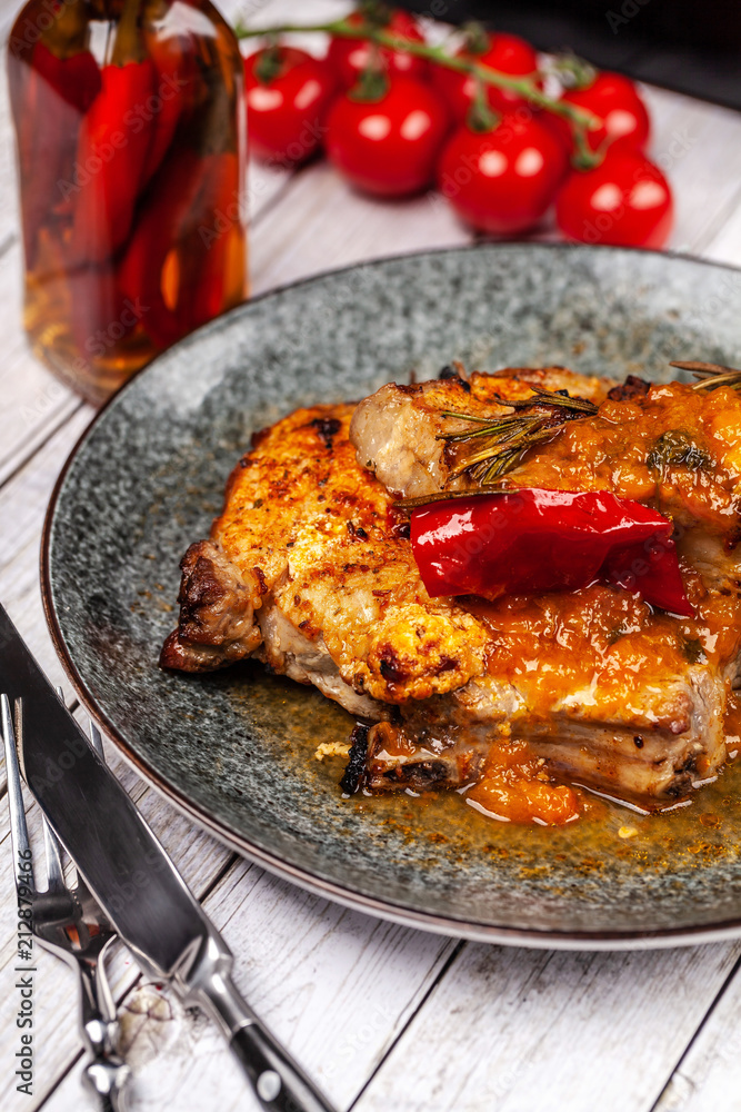 Mexican cuisine, pork or beef steak with a spicy sauce of salsa. with red pepper, marasm and titanium, cherry tomatoes, knife and fork. Mexican cuisine, pork or beef steak with a spicy sauce of salsa. with red pepper, marasm and titanium, cherry tomatoes, knife and fork.