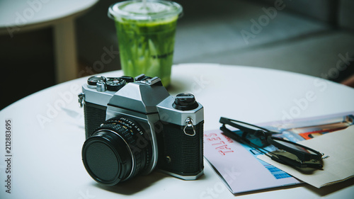 Camera wirh Green tea matcha atte in plastic cup and glasses and travel book on the table in cafe. photo