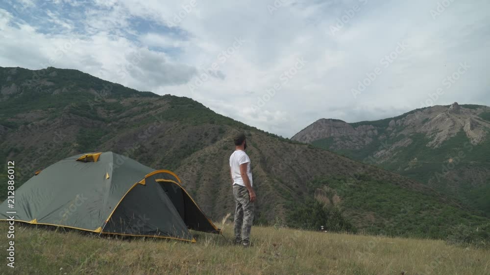 Mountains and hills, men traveler comes out of tourist tent near mountain valley.
Mountains and hills, men traveler comes out of tourist tent near mountain valley.