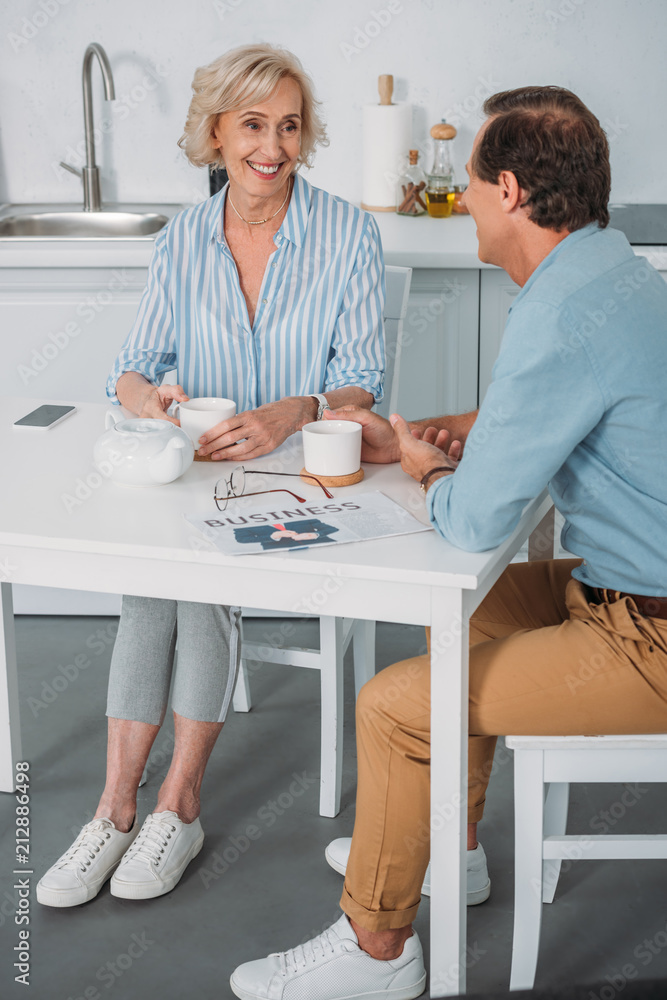 happy senior couple smiling each other and talking while drinking tea together at home happy senior couple smiling each other and talking while drinking tea together at home