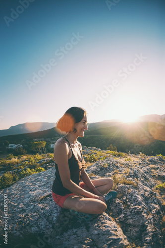 The girl is sitting on the top of the mountain at sunset.