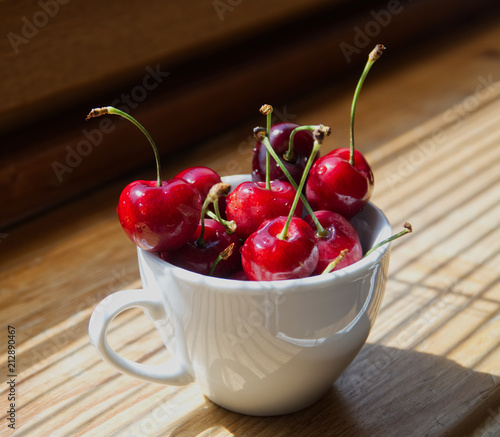 Cherry berries in a white cup on a wooden background with a light from the window