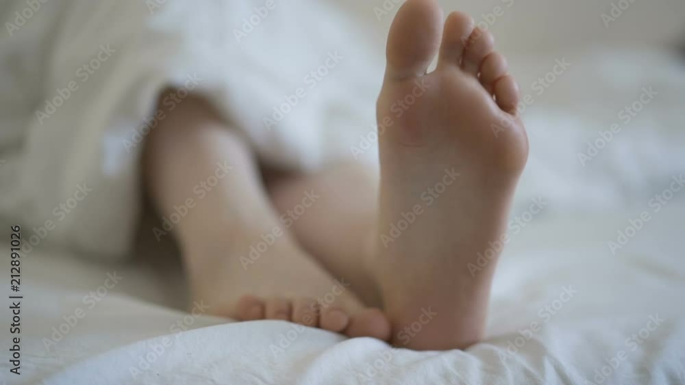 Delicate female feet moving toes playfully on white bedding Delicate female feet moving toes playfully on white bedding