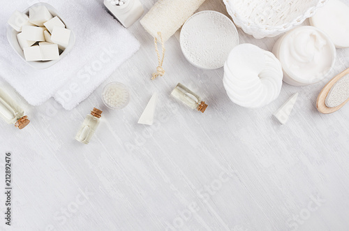 Soft pure white cosmetics set and bath accessories on light soft wooden background, flat lay.