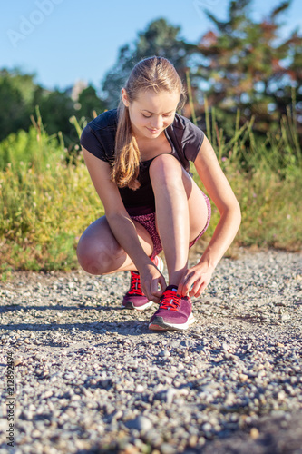 Sport and fitness. Young woman training outdoor is going to tie shoelaces.