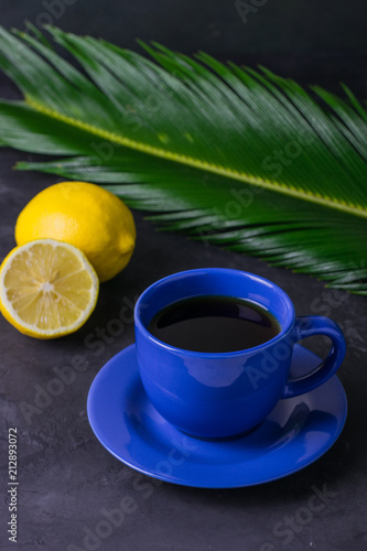 A blue cup of tea, a lemon and a green leaf on a dark table