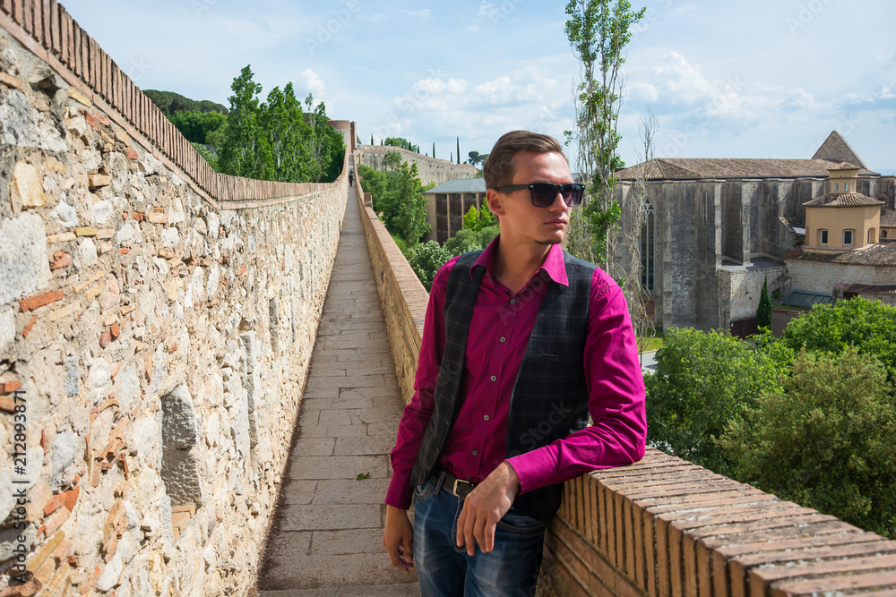 A young tourist with a backpack standing on a Fortress wall (Passeig de la Murala) in Girona, Spain. A young tourist with a backpack standing on a Fortress wall (Passeig de la Murala) in Girona, Spain.