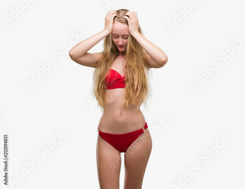 Blonde teenager woman wearing red bikini suffering from headache desperate and stressed because pain and migraine. Hands on head.