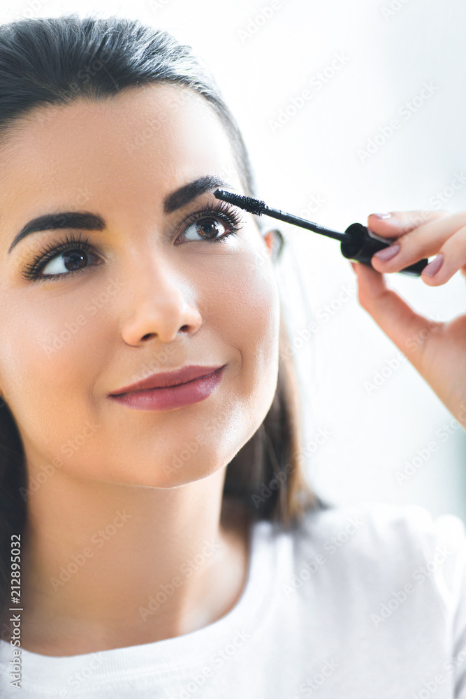 portrait of attractive young woman applying black mascara on eyelashes