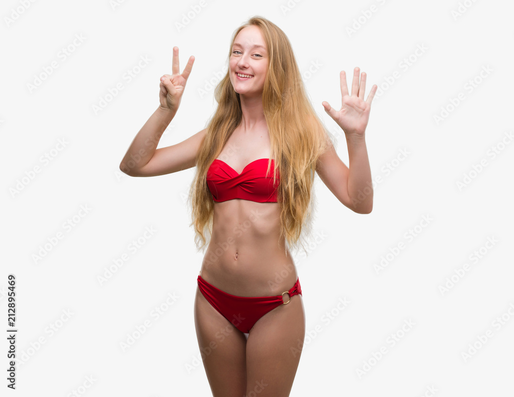 Blonde teenager woman wearing red bikini showing and pointing up with fingers number seven while smiling confident and happy.