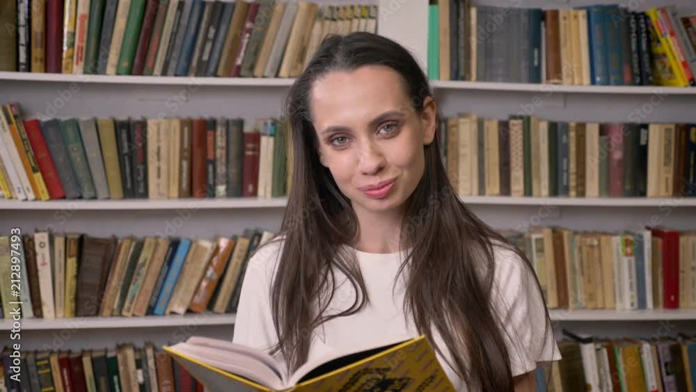 Young sexy brunette girl is reading book in library, watchinf at camera, smiling Young sexy brunette girl is reading book in library, watchinf at camera, smiling