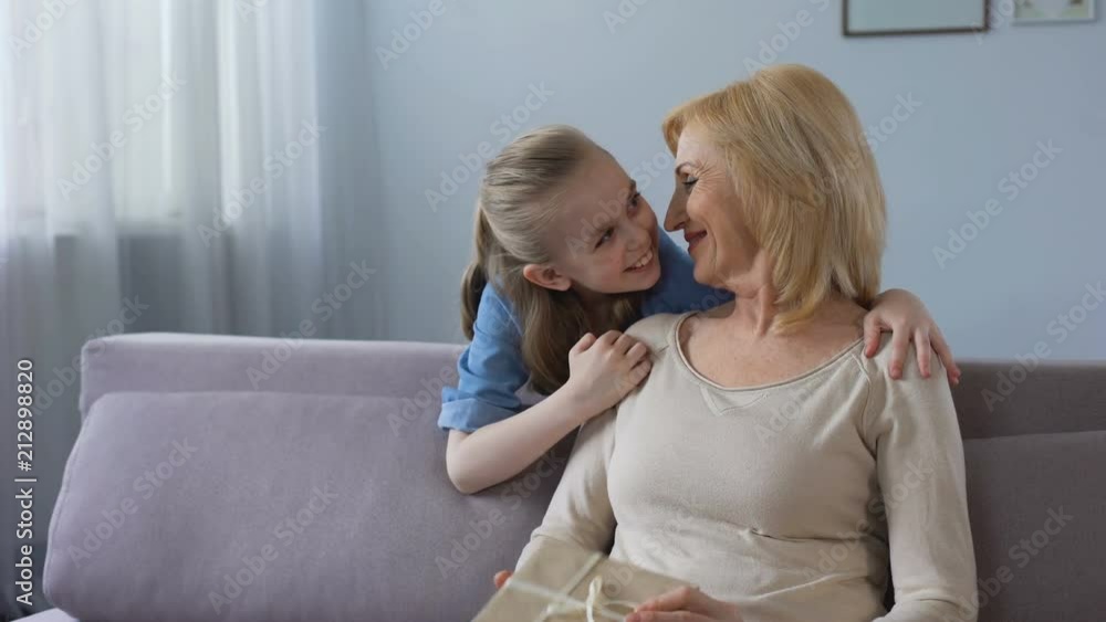 Cute granddaughter giving gift to grandmother and hugging her, family love Cute granddaughter giving gift to grandmother and hugging her, family love