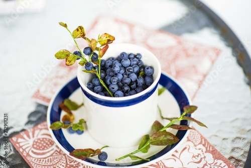 Bleberries in cup and plate on glass table.