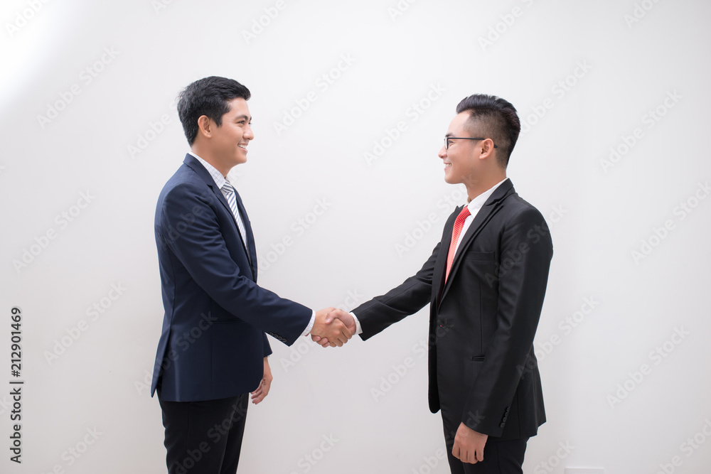 Side view of two smiling young businessmen shaking hands in white background Side view of two smiling young businessmen shaking hands in white background