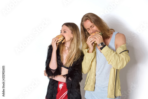 hungry young couple eating tasty burgers on white
