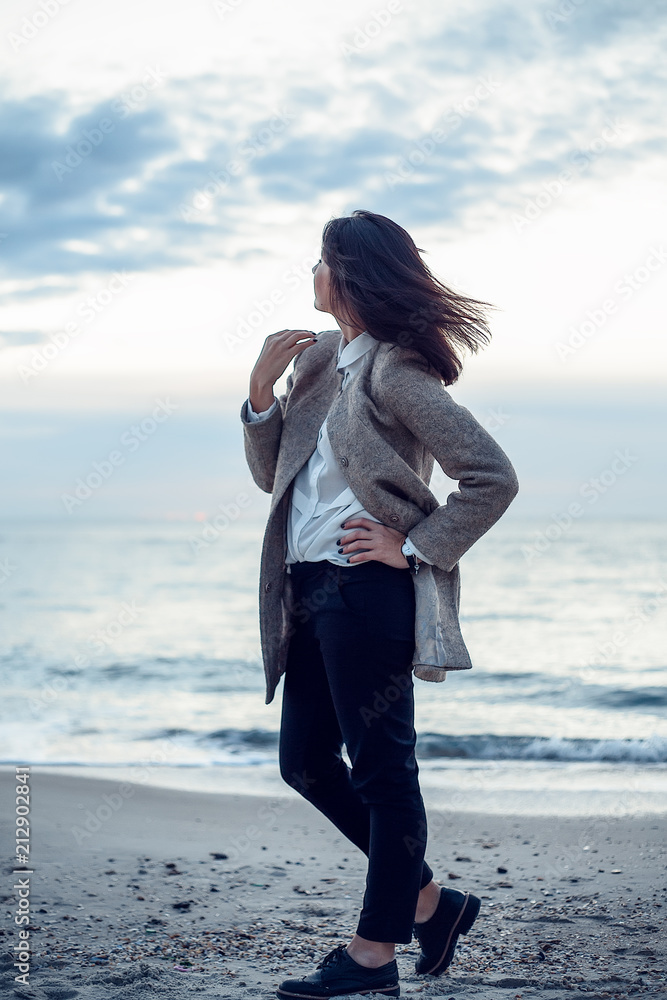Woman in coat and trousers walking by seashore with flying seagulls Woman in coat and trousers walking by seashore with flying seagulls