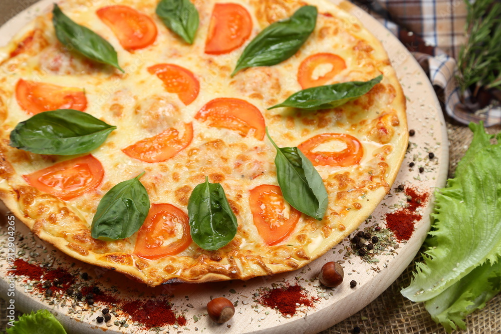 Pizza with tomato, cheese, salad, on a wooden stand closeup Pizza with tomato, cheese, salad, on a wooden stand closeup
