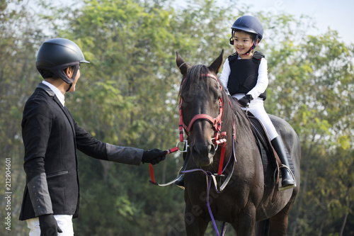 Young Chinese father teaching daughter riding horse