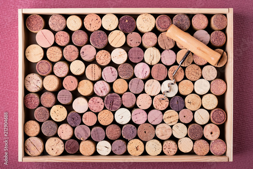 Wine cork stoppers in wooden box and corkscrew on Fuchsia background Copy space