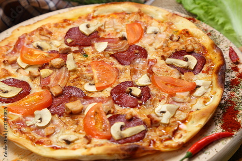 Pizza with mushrooms, tomato, smoked sausage, bacon, red pepper and cheese close-up