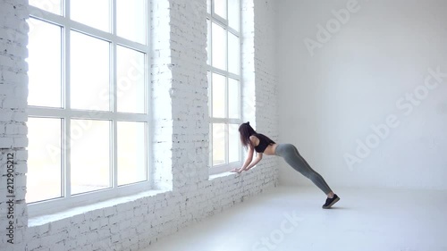 Fitness woman in sportwear is waming up by doing ups on the window sill. Studio location. 4k. photo