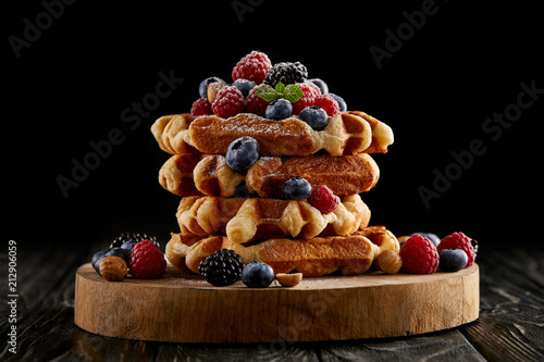 freshly baked stack of belgian waffles with berries on wooden cutting board on black