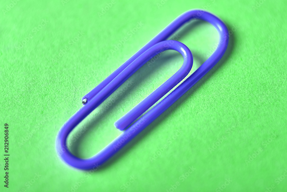 One blue paper clip isolated on green background, close up, copy space. Top view, flat lay. Back to school, college, education concept One blue paper clip isolated on green background, close up, copy space. Top view, flat lay. Back to school, college, education concept