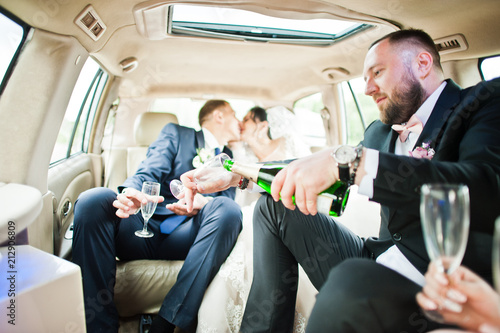 Groomsman opening the bottle and pouring champagni into glasses in the car.
