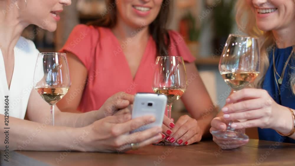 people, technology and lifestyle concept - happy women with smartphone drinking wine at bar or restaurant people, technology and lifestyle concept - happy women with smartphone drinking wine at bar or restaurant