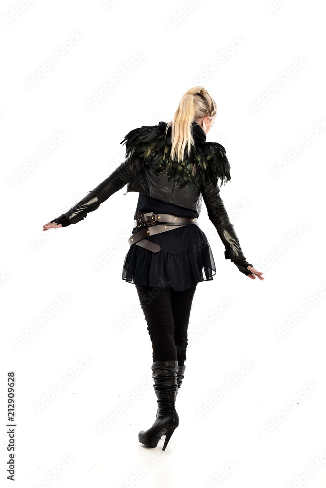 full length portrait of blonde girl wearing lack fantasy warrior outfit. standing pose wit bak to the camera. isolated on white studio background.