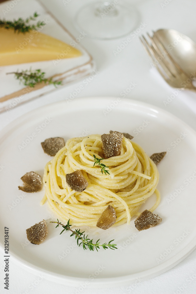 Pasta with creamy cheese sauce and truffle on a light plate, served with cheese and wine.