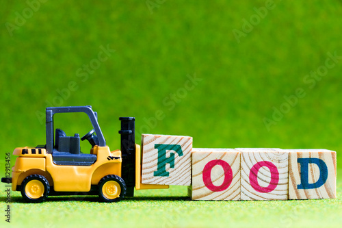 Toy forlift hold letter block f to fulfill word food on green background photo