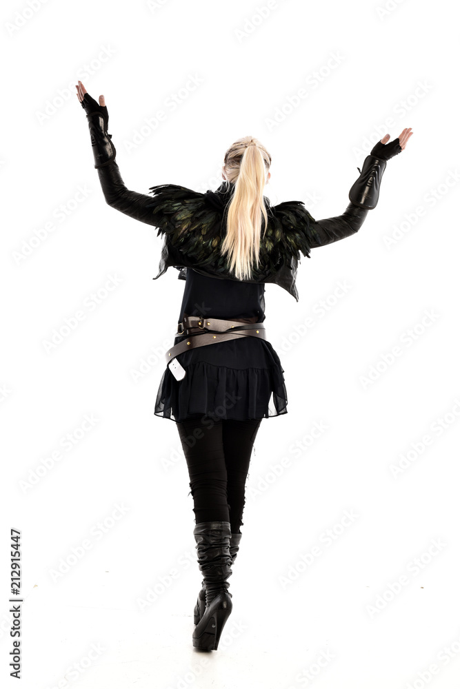 full length portrait of blonde girl wearing lack fantasy warrior outfit. standing pose wit bak to the camera. isolated on white studio background. full length portrait of blonde girl wearing lack fantasy warrior outfit. standing pose wit bak to the camera. isolated on white studio background.
