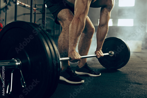 Fotografie Fit young man lifting barbells working out in a gym