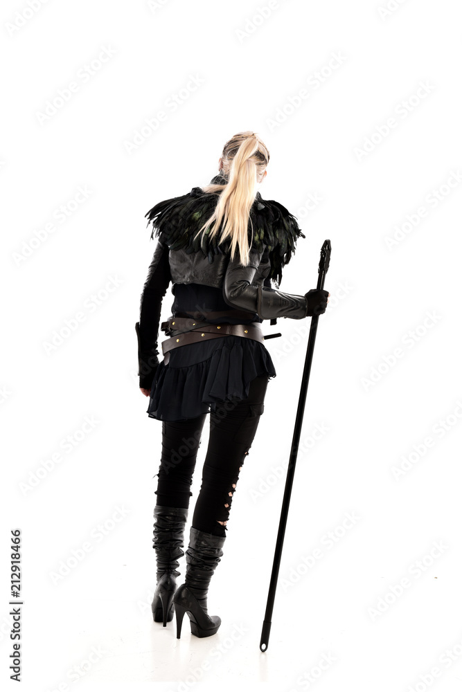 full length portrait of blonde girl wearing lack fantasy warrior outfit. standing pose wit bak to the camera. isolated on white studio background. full length portrait of blonde girl wearing lack fantasy warrior outfit. standing pose wit bak to the camera. isolated on white studio background.