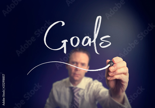 A businessman writing a goals concept with a white pen on a clear screen.