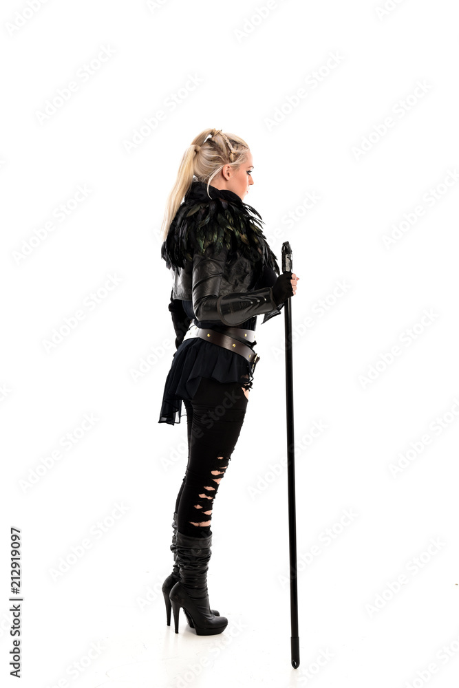 full length portrait of blonde girl wearing lack fantasy warrior outfit. standing pose wit bak to the camera. isolated on white studio background. full length portrait of blonde girl wearing lack fantasy warrior outfit. standing pose wit bak to the camera. isolated on white studio background.
