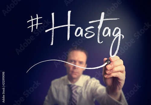 A businessman writing a hashtag concept with a white pen on a clear screen.