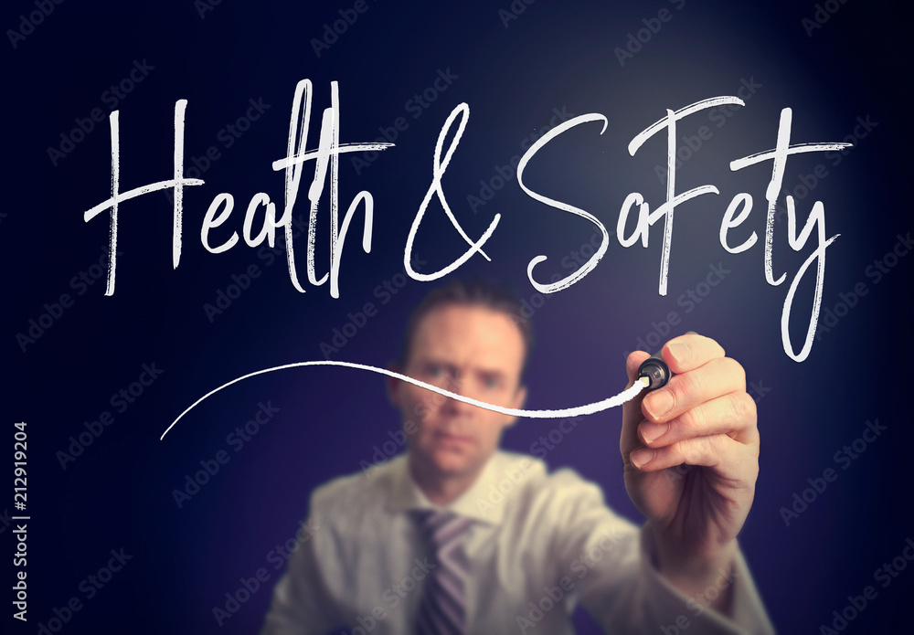 A businessman writing a health and safety concept with a white pen on a clear screen. A businessman writing a health and safety concept with a white pen on a clear screen.
