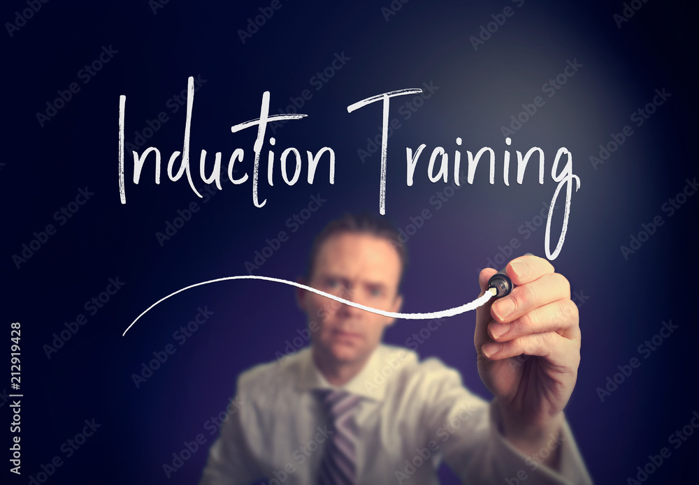 A businessman writing a induction training concept with a white pen on a clear screen. A businessman writing a induction training concept with a white pen on a clear screen.