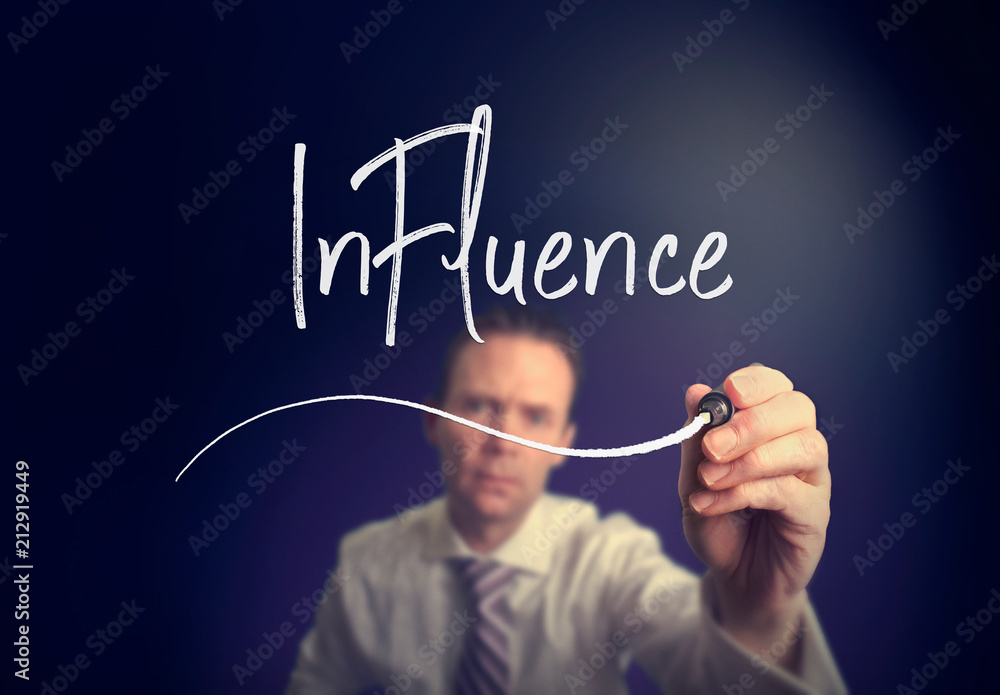 A businessman writing a influence concept with a white pen on a clear screen. A businessman writing a influence concept with a white pen on a clear screen.