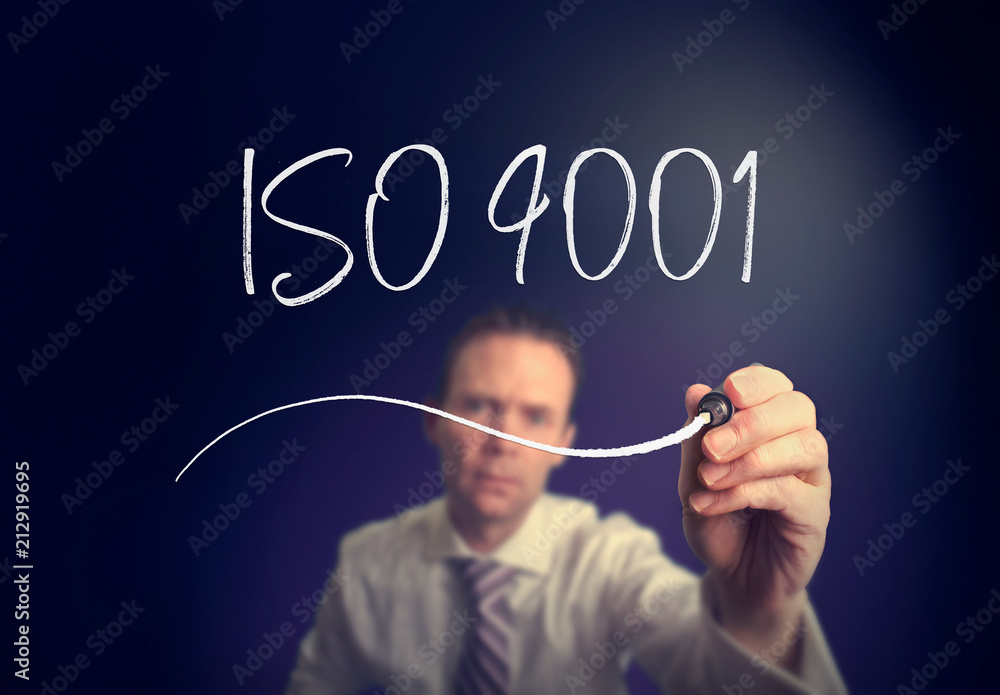 A businessman writing a iso 9001 concept with a white pen on a clear screen. A businessman writing a iso 9001 concept with a white pen on a clear screen.