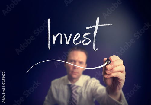 A businessman writing a invest concept with a white pen on a clear screen.