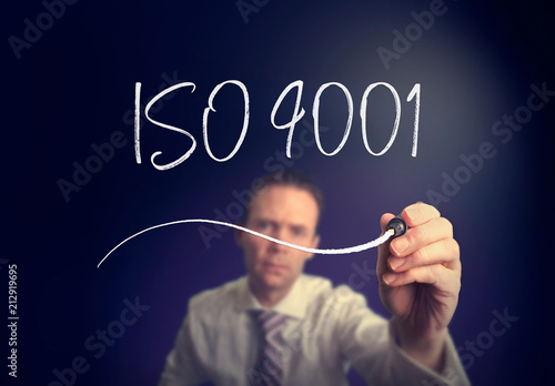 A businessman writing a iso 9001 concept with a white pen on a clear screen.