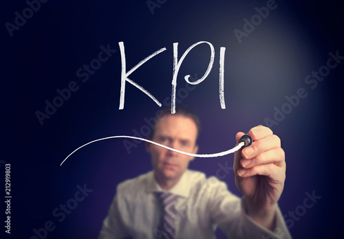 A businessman writing a KPI concept with a white pen on a clear screen.