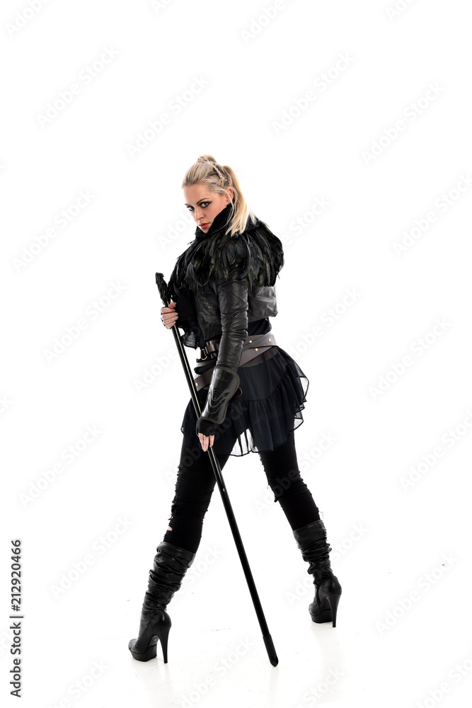 full length portrait of blonde girl wearing lack fantasy warrior outfit. standing pose wit bak to the camera. isolated on white studio background.