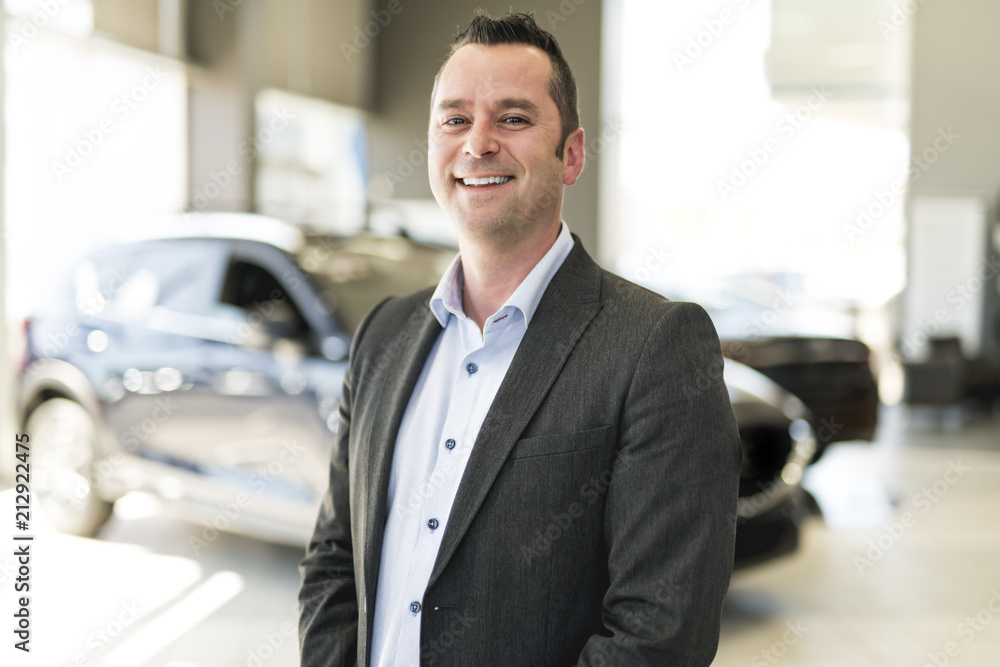 Business man working at a car dealer smiling Business man working at a car dealer smiling