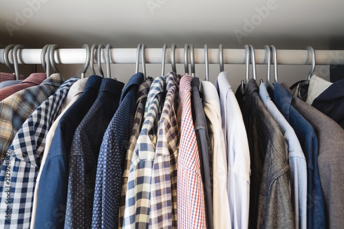 Various shirts hanging in hangers at home photo