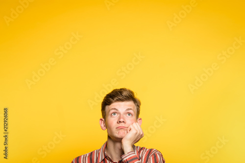 bored disinterested weariful indifferent unenthusiastic man looking up. hand under his chin. portrait of a young guy on yellow background pop up or peek out from bottom. copy space for advertisement. photo